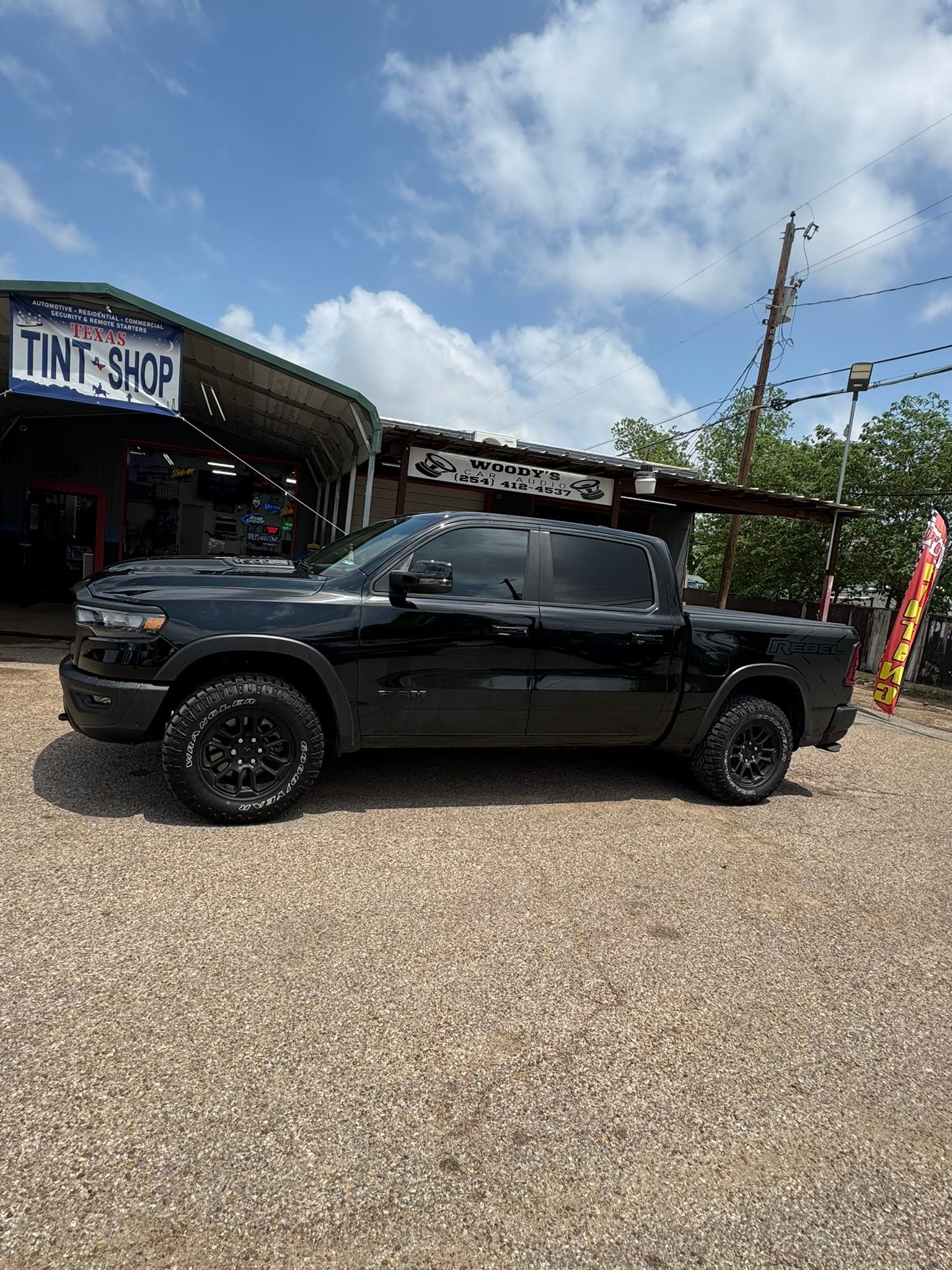 A black truck is parked in a gravel lot in front of a building.