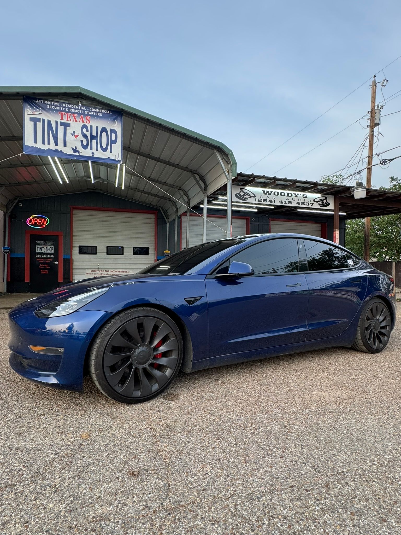 A blue tesla model 3 is parked in front of a tint shop.