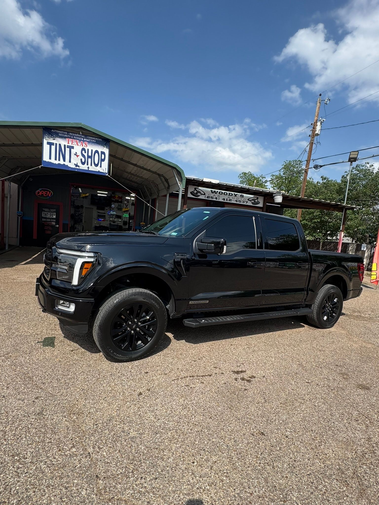 A black pickup truck is parked in front of a tint shop.