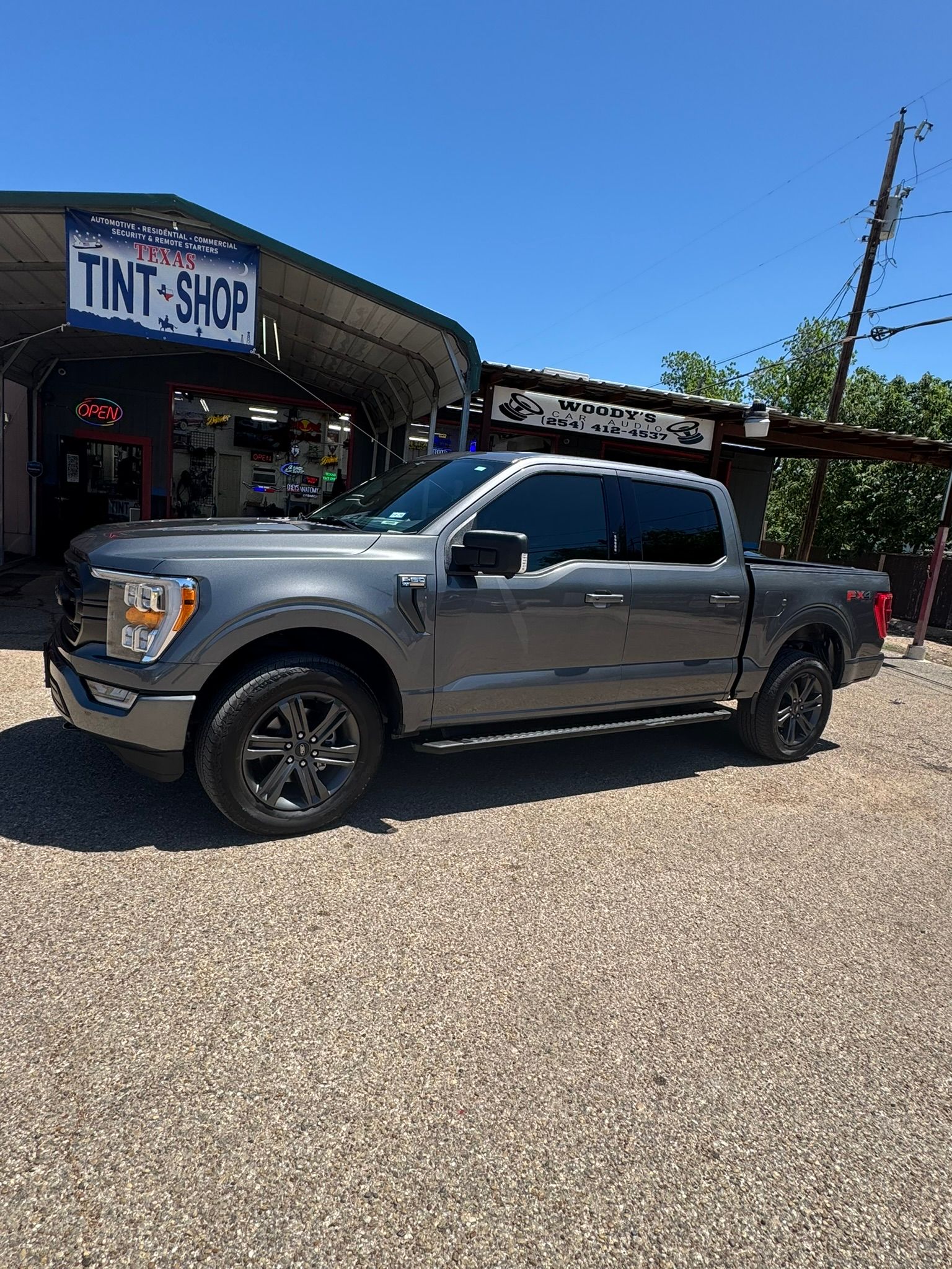 A gray pickup truck is parked in front of a tint shop.