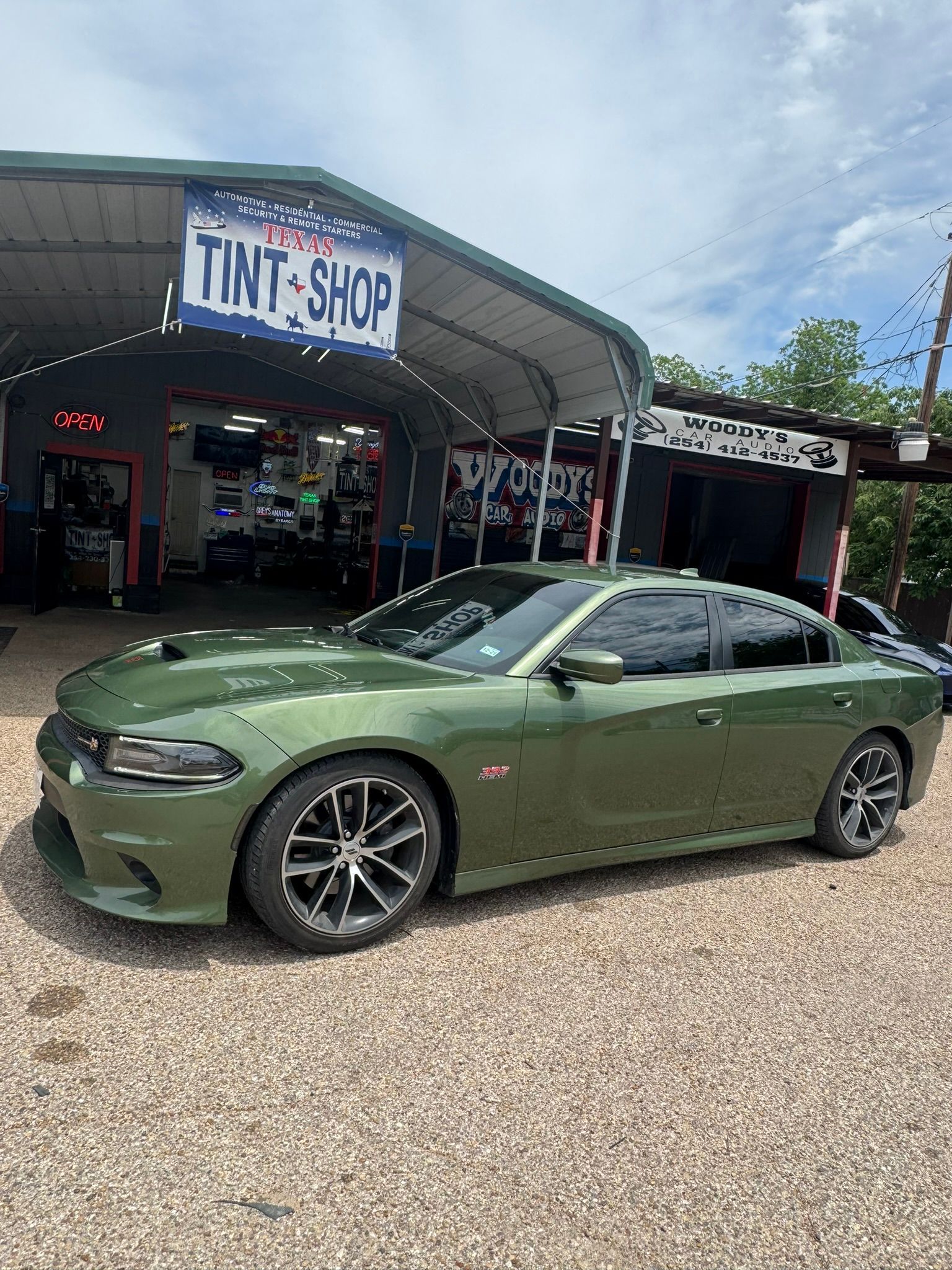 A green dodge charger is parked in front of a tint shop.