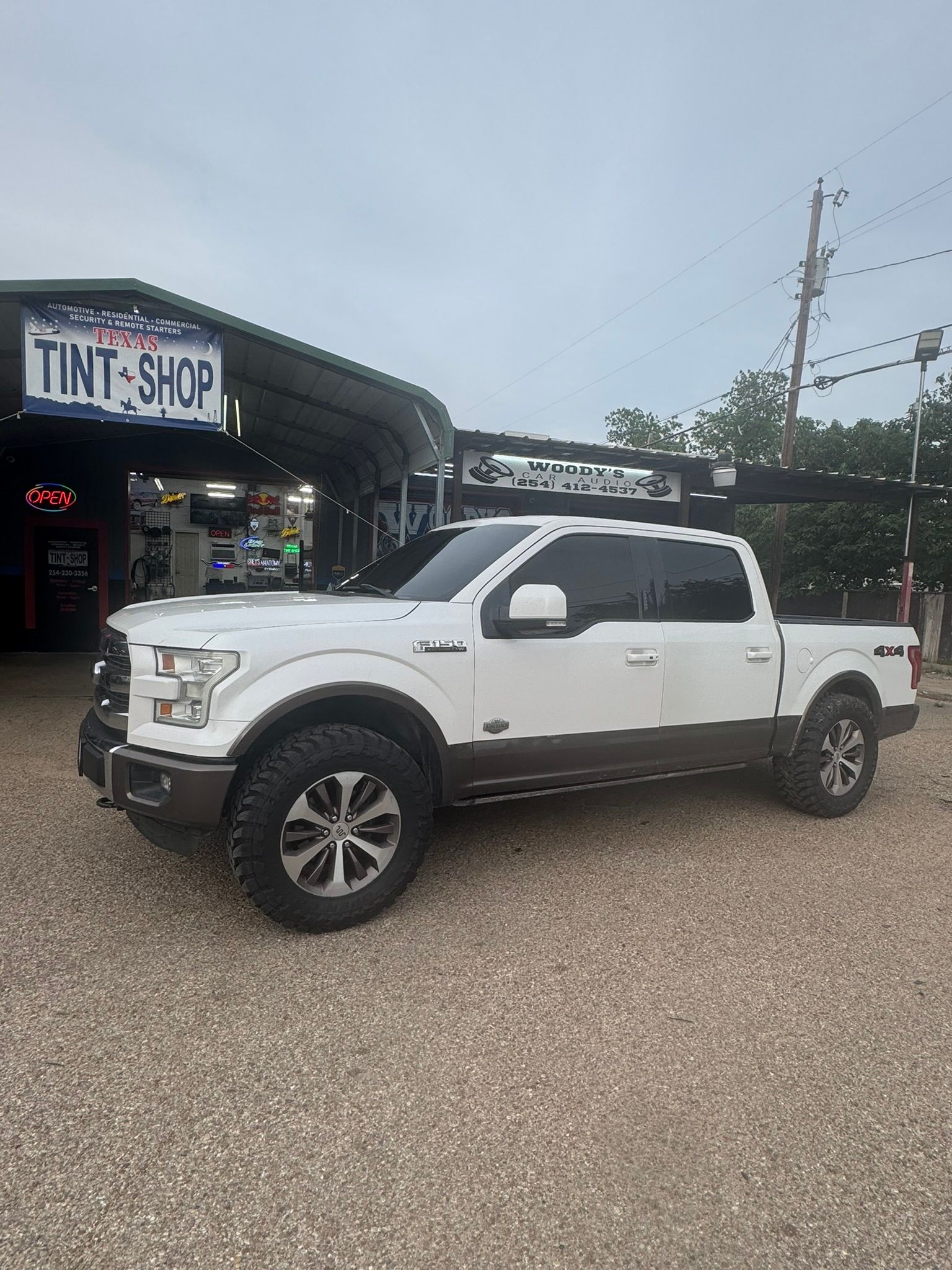 A white pickup truck is parked in front of a tint shop.
