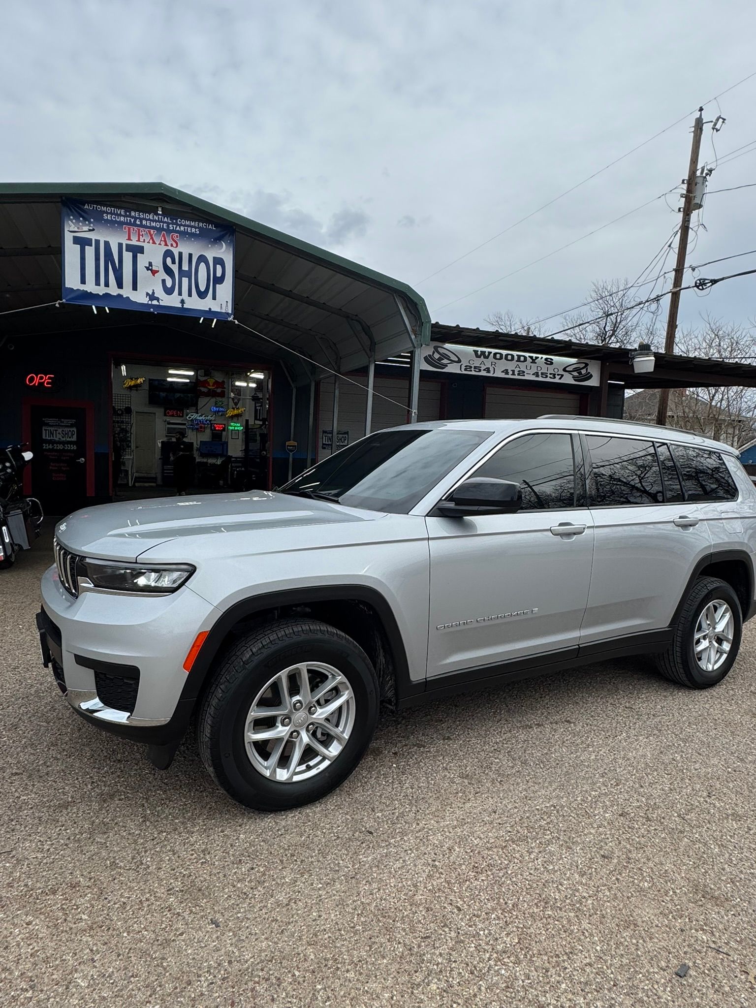 A silver jeep grand cherokee is parked in front of a tint shop.