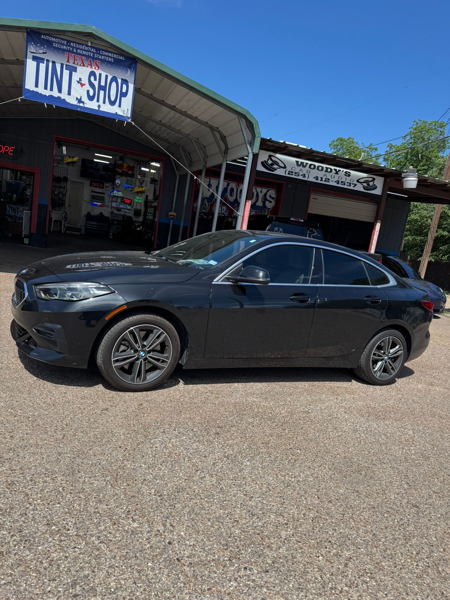 A black car is parked in front of a tint shop.