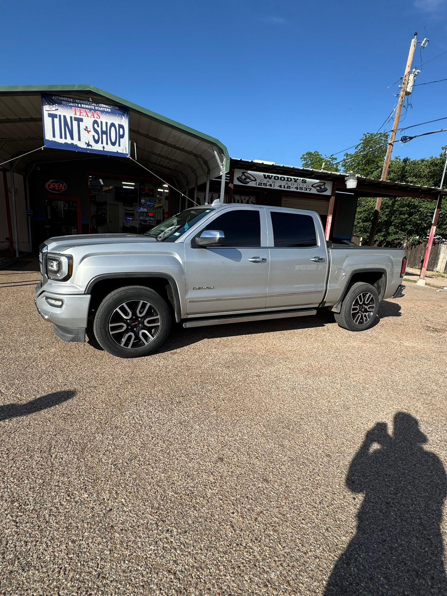 A silver truck is parked in a gravel lot in front of a building.