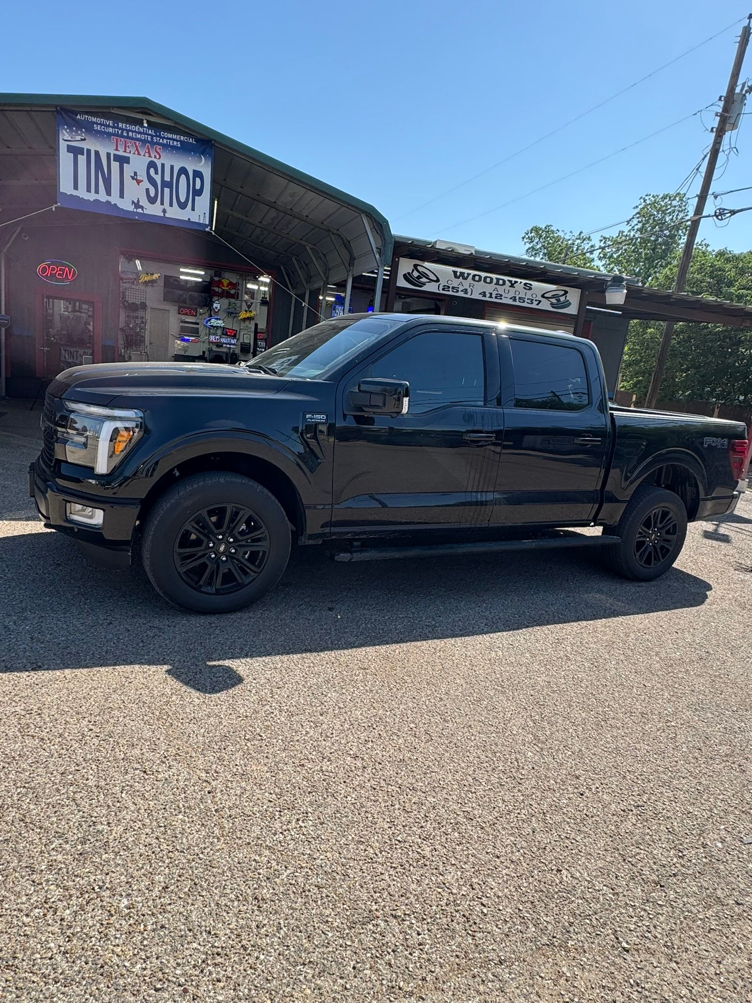 A black pickup truck is parked in front of a tint shop.
