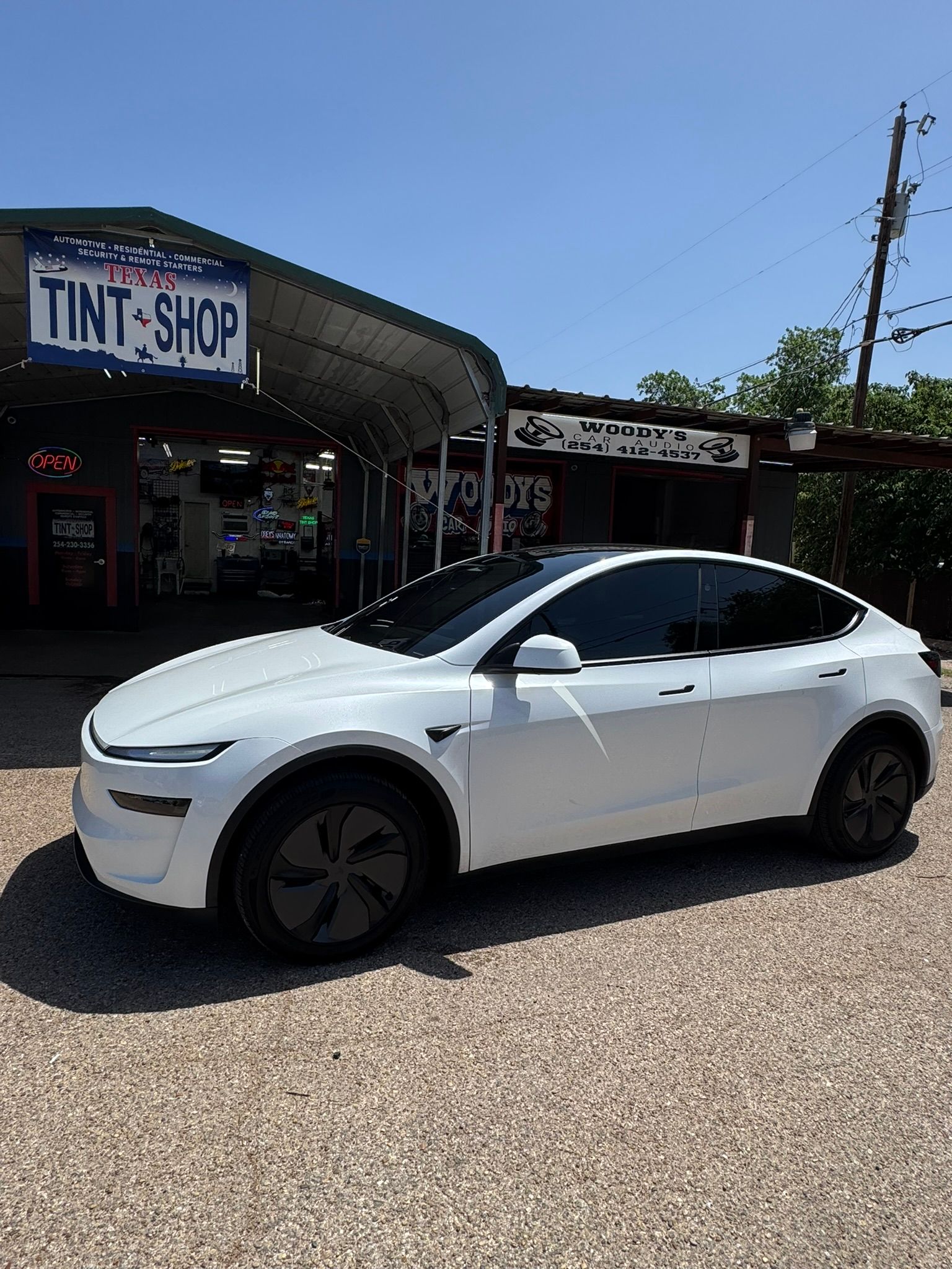 A white tesla model x is parked in front of a tint shop.