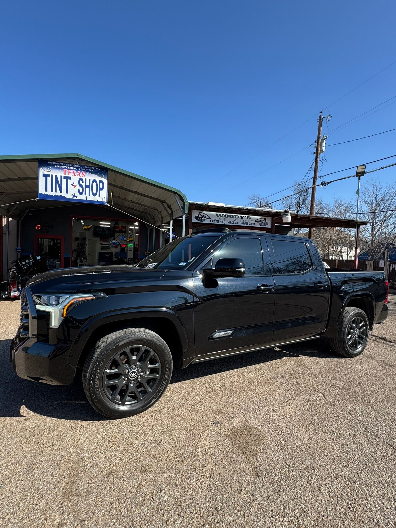 A black truck is parked in front of a tint shop.