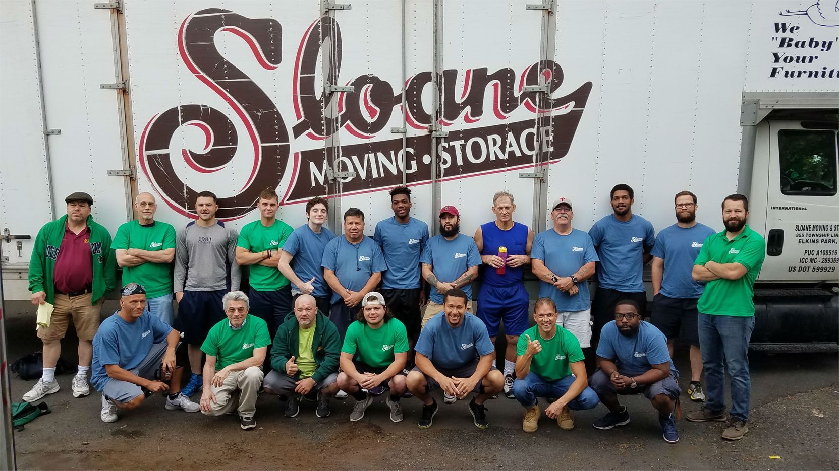 Group of movers in blue and green shirts pose in front of a truck.
