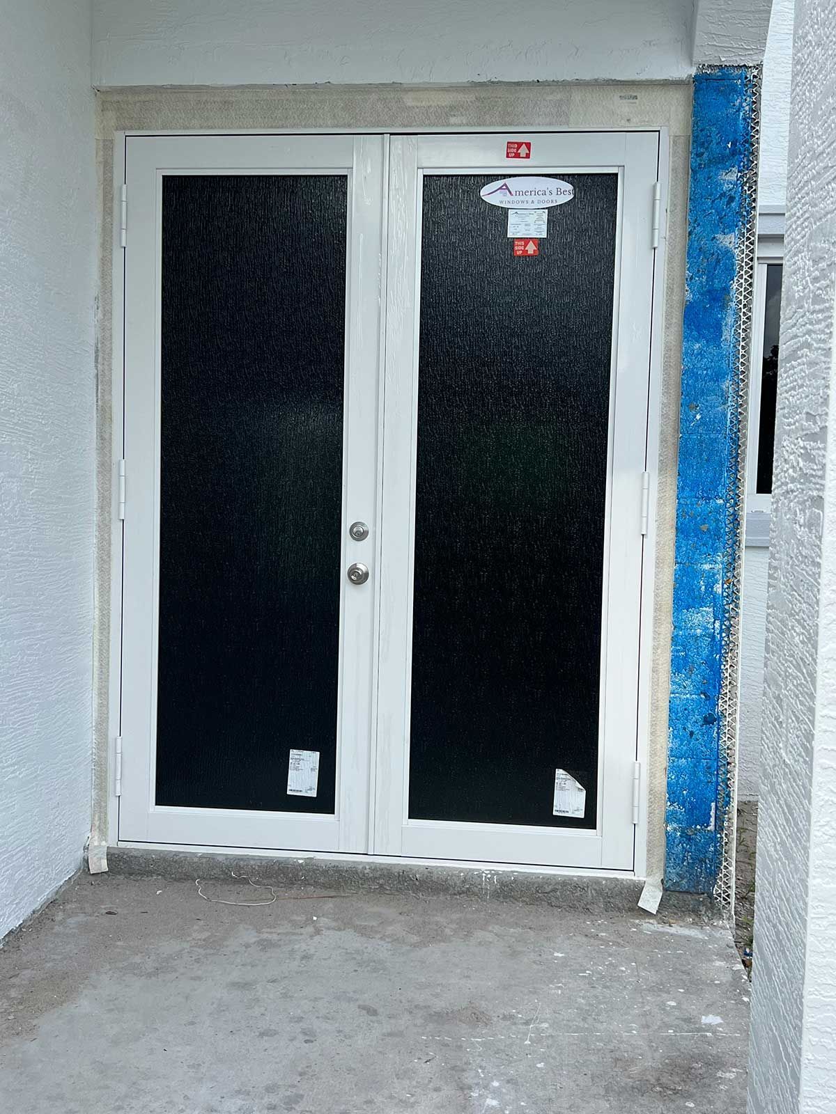 A white door with black glass is sitting on a concrete floor.