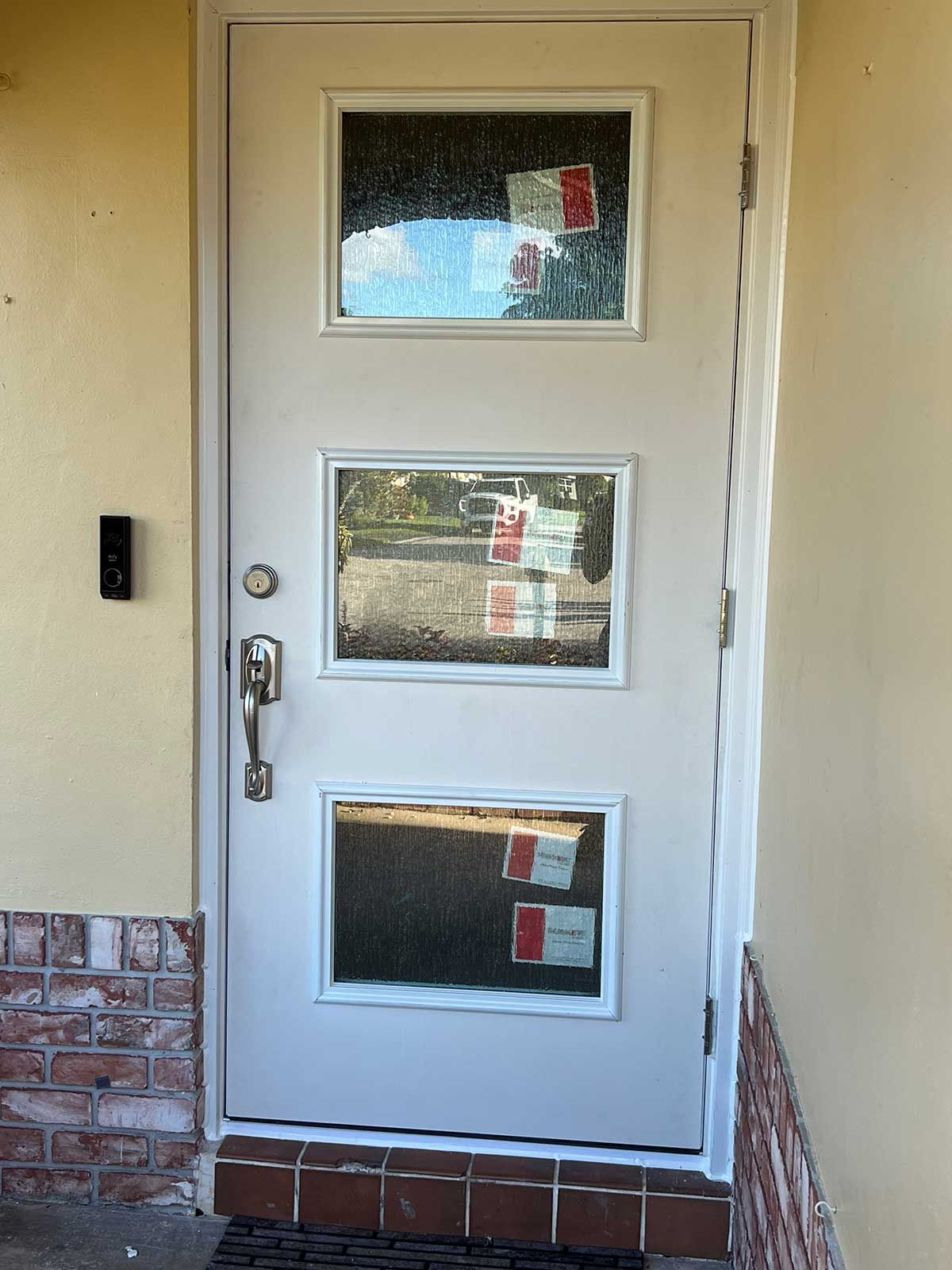 A white door with three square windows on a brick wall.