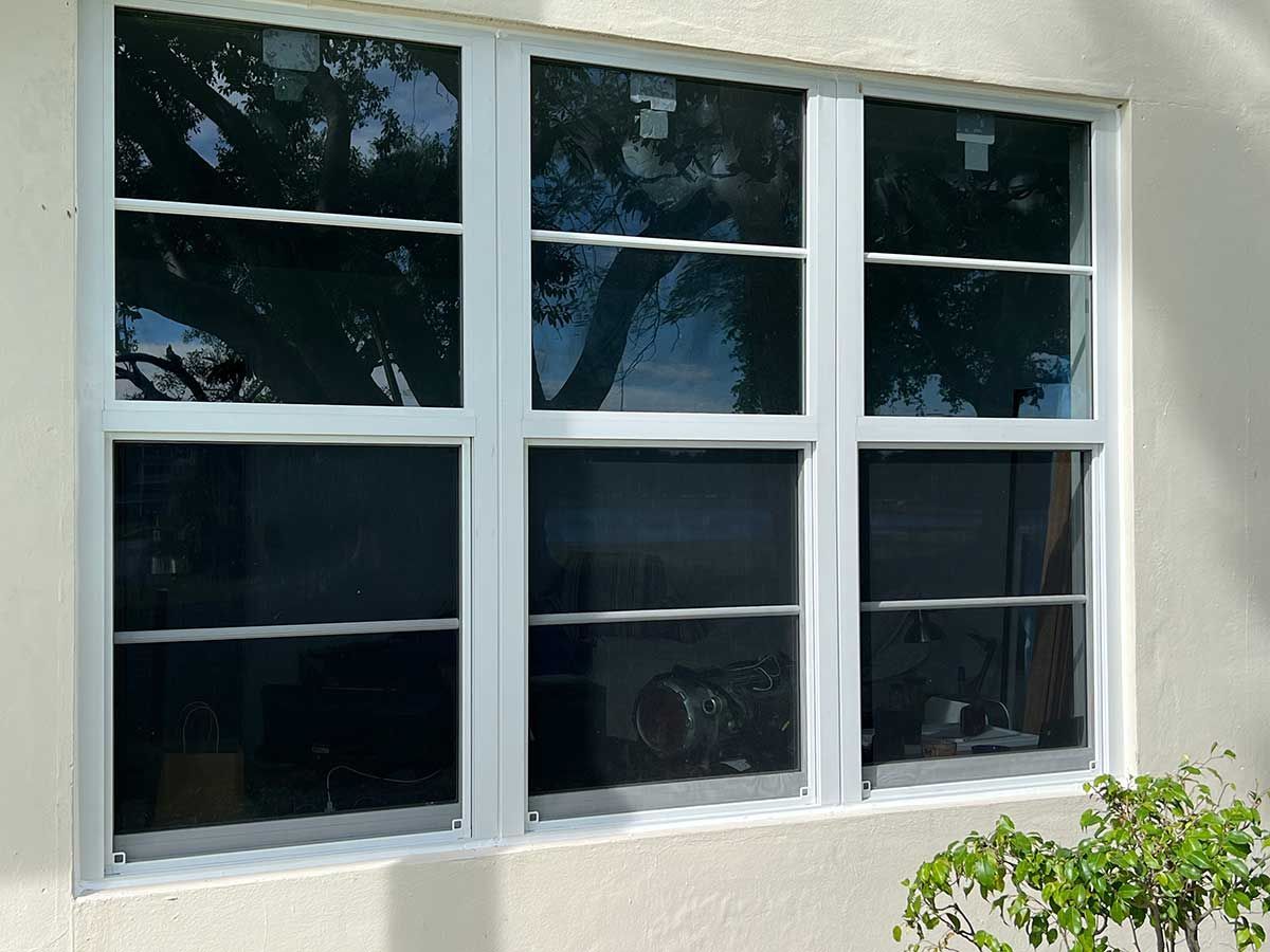 A white house with three windows and a tree in the background.