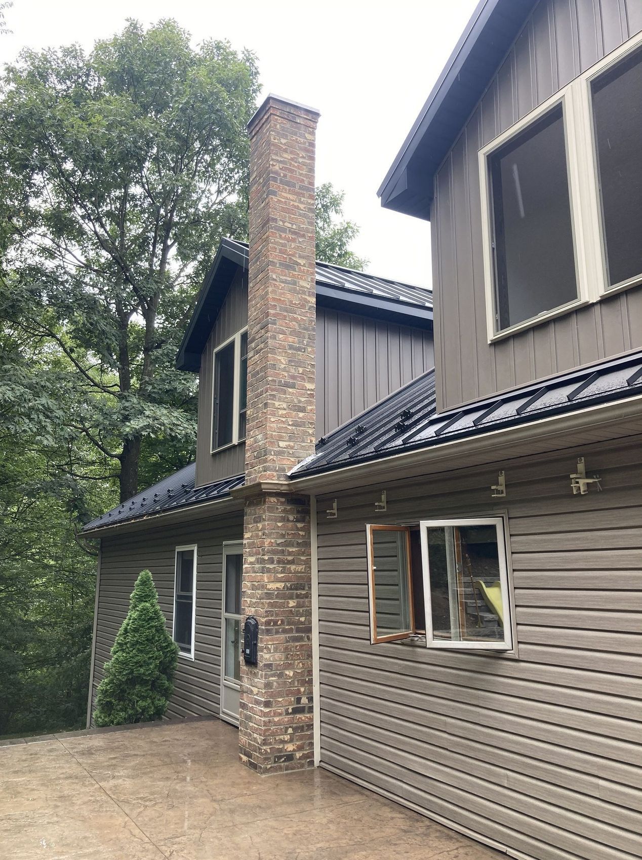 A multi-level home with grey horizontal and vertical siding, a stone chimney, and a dark metal roof.