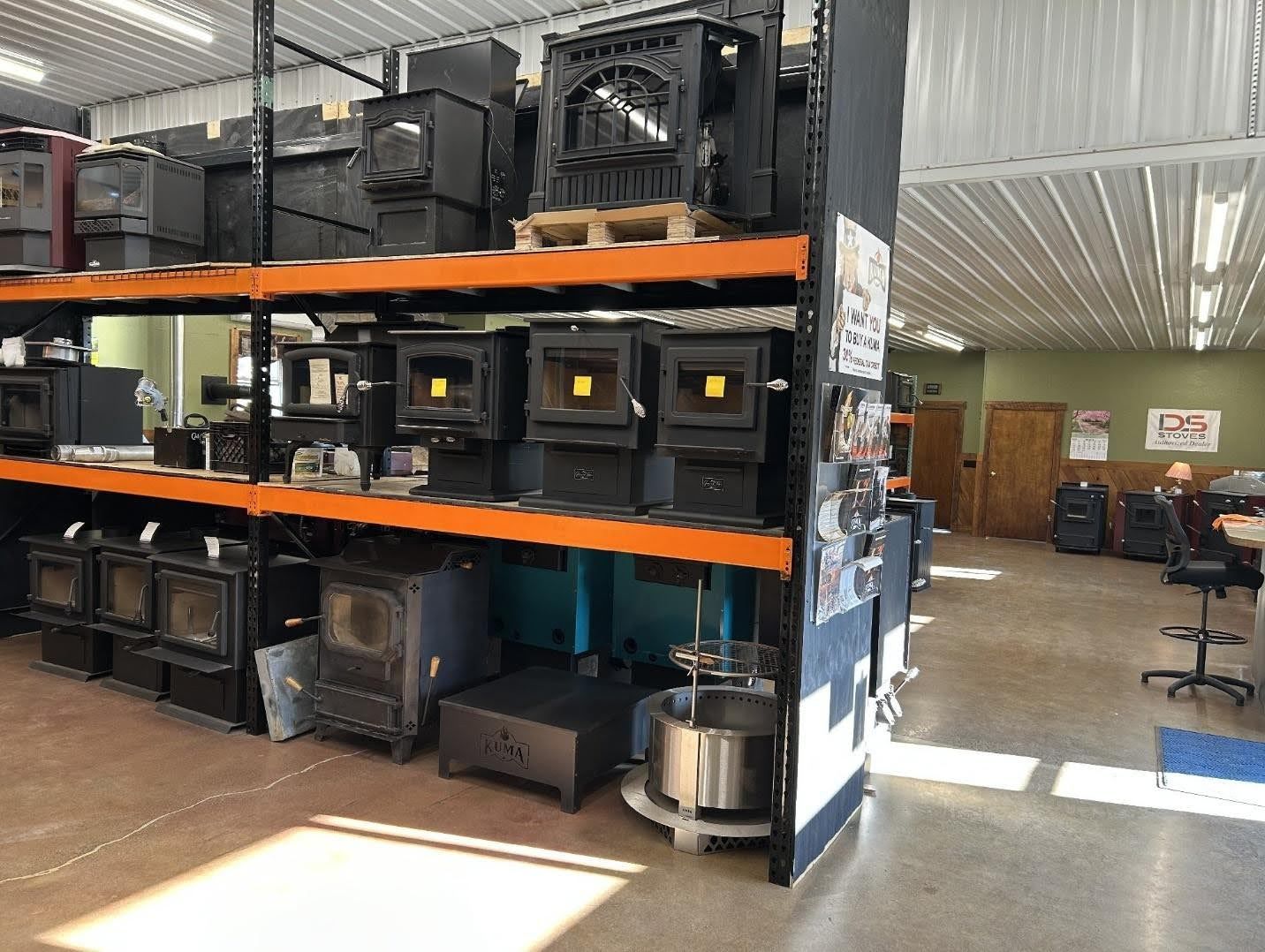 A retail showroom with various wood-burning and pellet stoves displayed on industrial metal shelving units.