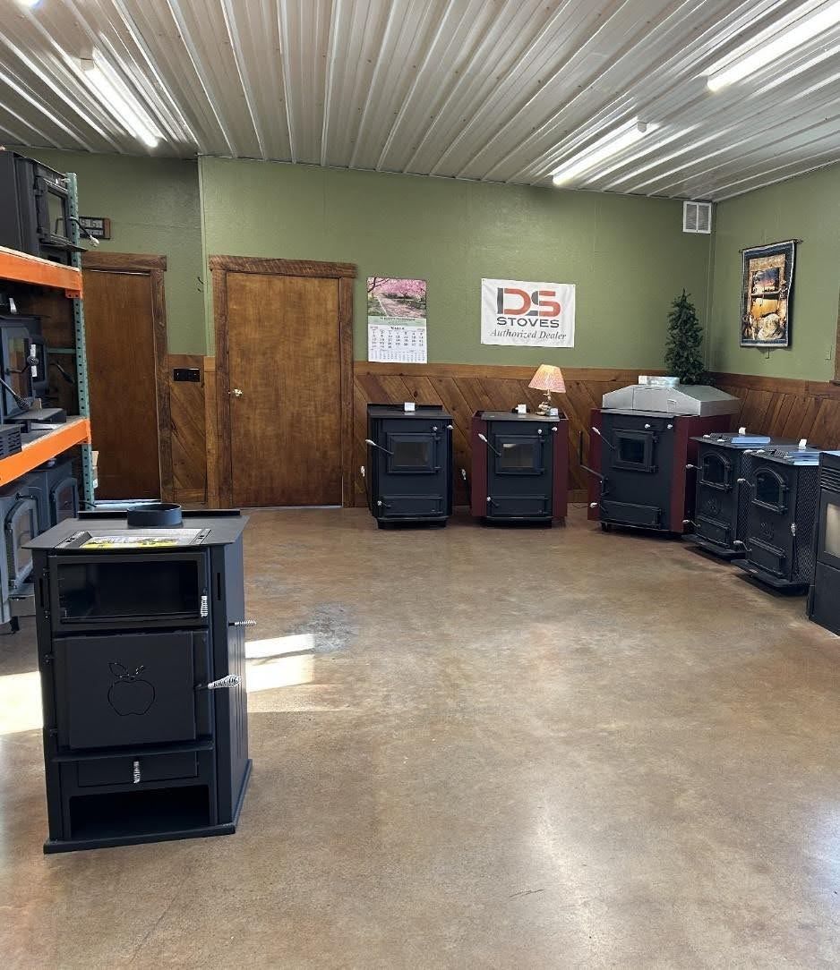 A showroom with several black coal stoves displayed on a concrete floor in front of green and wood-paneled walls.