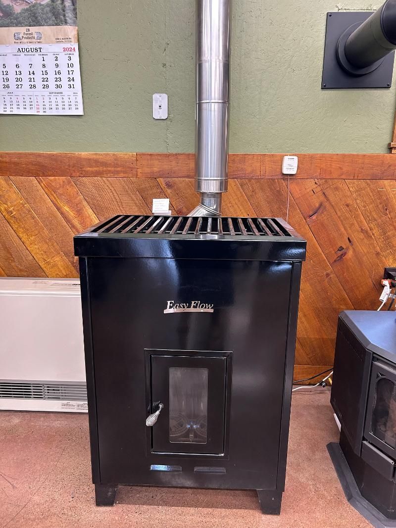 Black wood-burning stove with a stainless steel chimney, in a room with wood paneling.