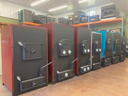 Row of wood-burning stoves in various colors and sizes, inside a warehouse.