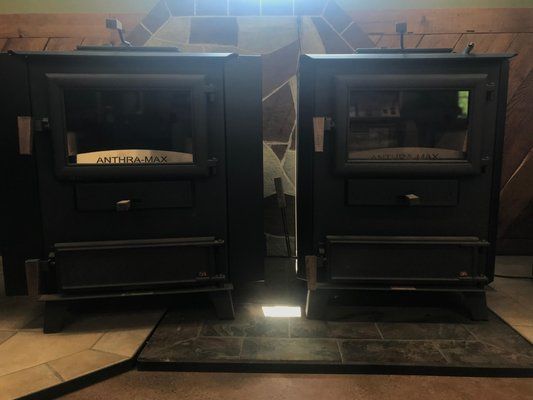 Two black wood-burning stoves with glass doors, side-by-side in a room.