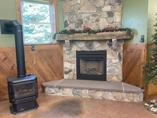 Stone fireplace with wood stove in room with window and wood paneling.