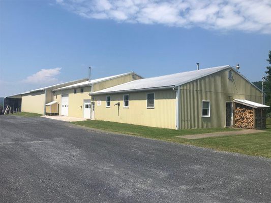 Yellow building with a gravel driveway, woodpile, and blue sky backdrop.