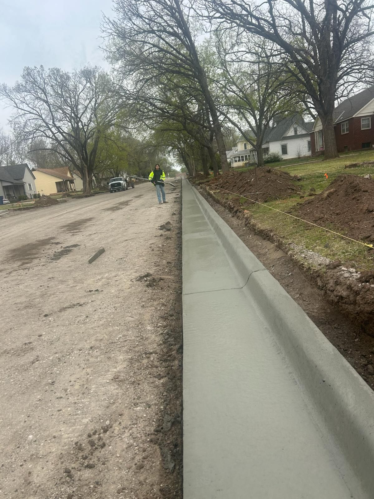 A man is walking down a dirt road next to a concrete curb.