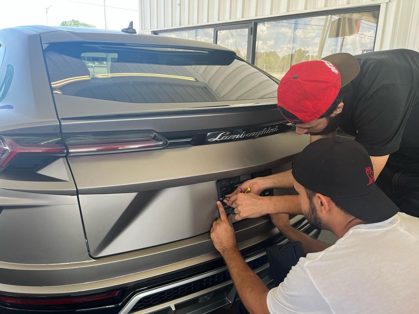 Two men are working on the back of a car.