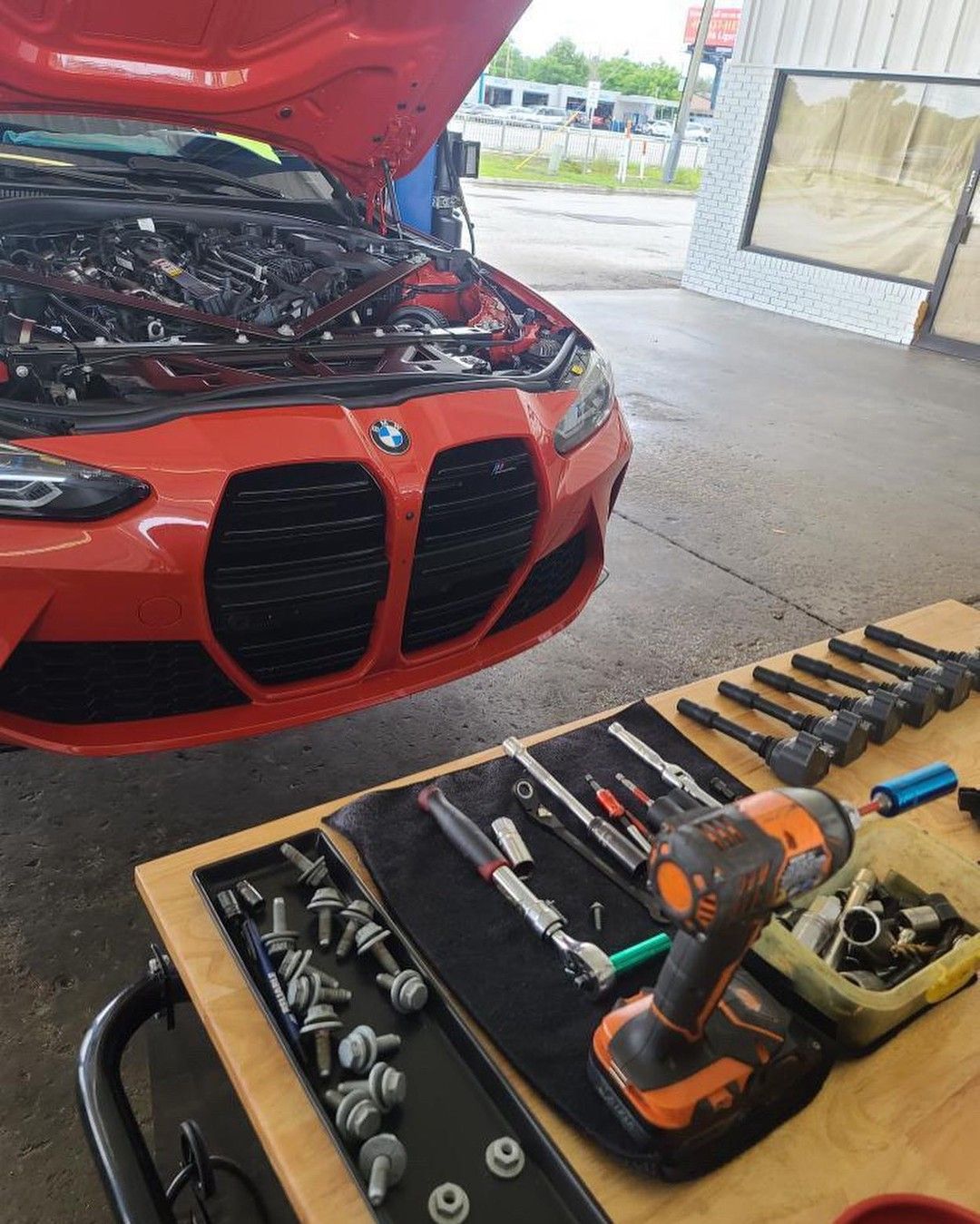 An orange bmw is being worked on with the hood open