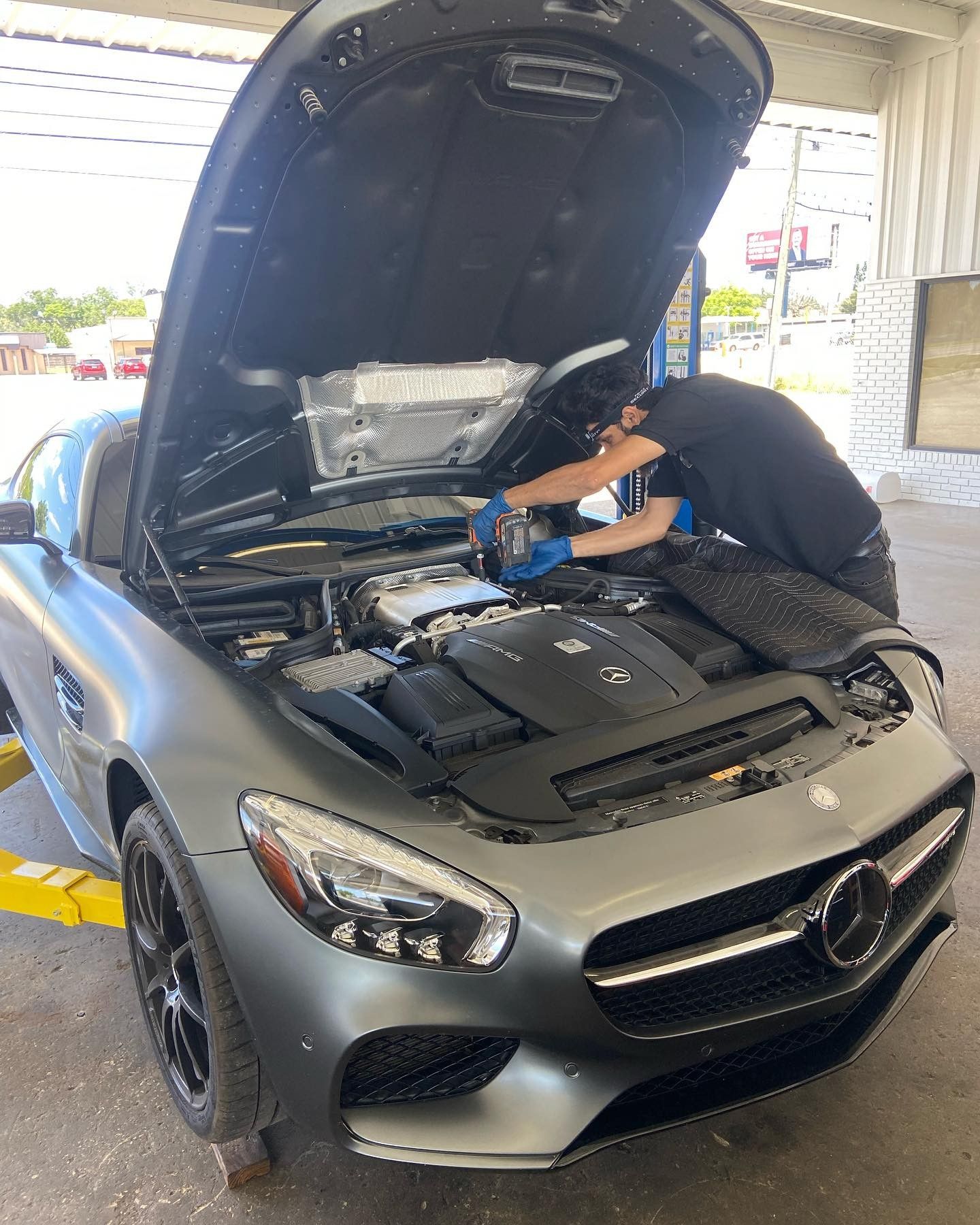 A man is working on the engine of a mercedes with the hood open.