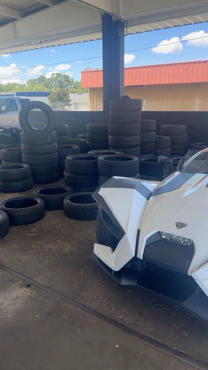 A white slingshot is parked in front of a pile of tires.