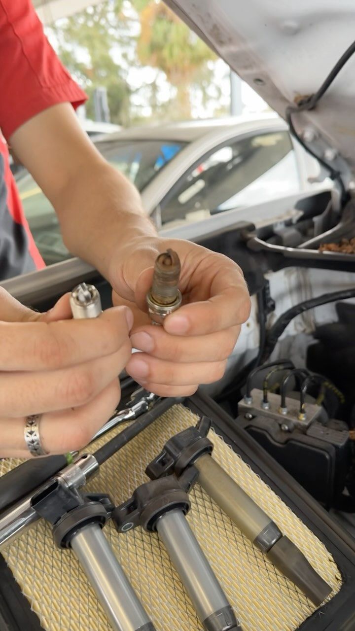 A person is holding a spark plug in their hand while working on a car.