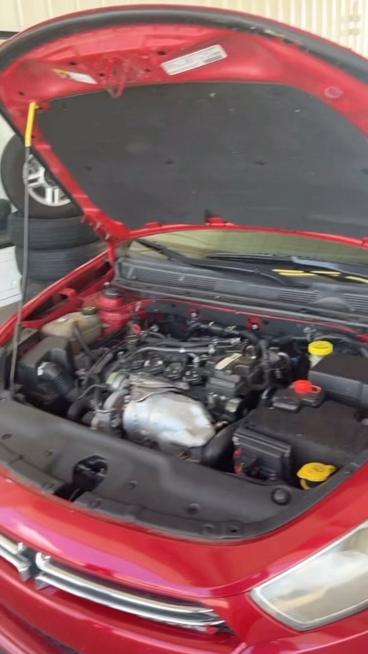The engine of a red car is shown with the hood open.