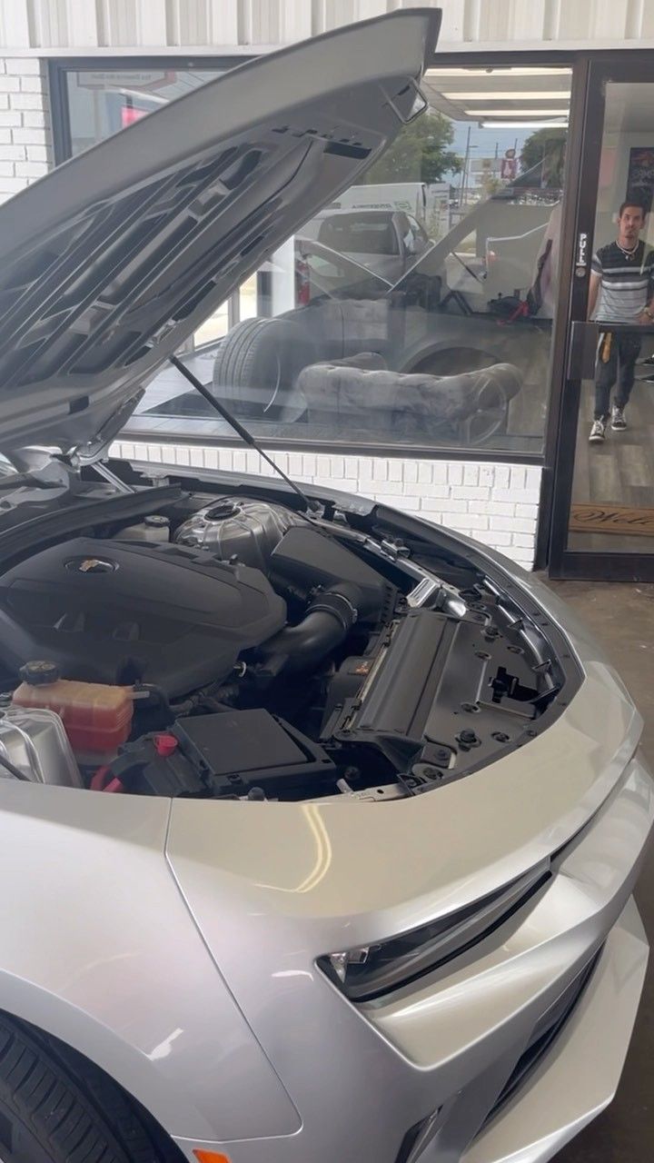 The hood of a silver car is open in a garage.