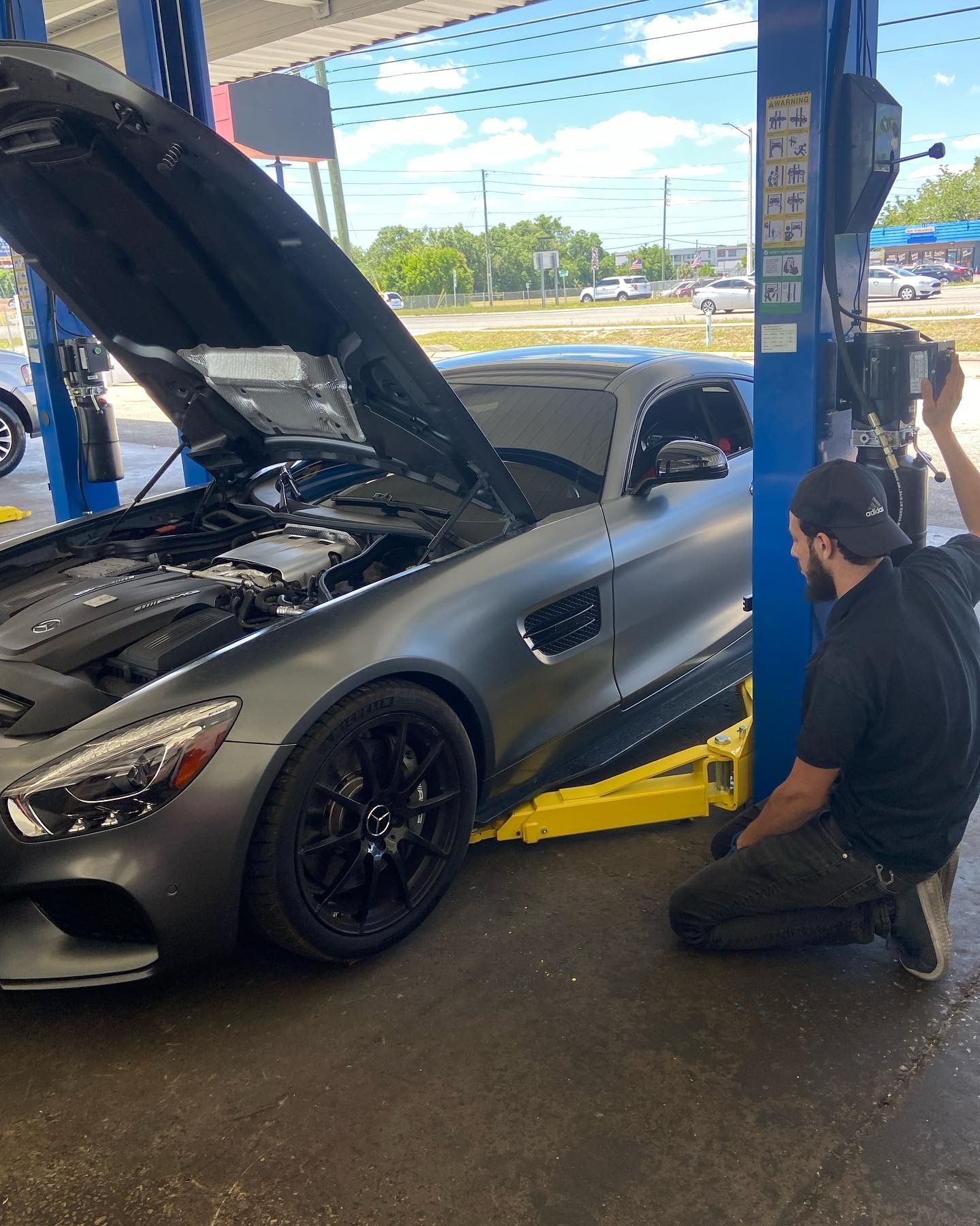 A man is kneeling next to a car with its hood up.