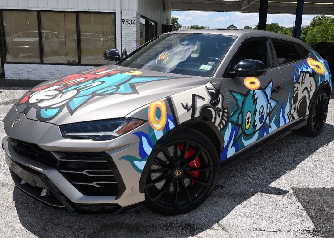 A lamborghini urus with graffiti painted on the side is parked in a parking lot.