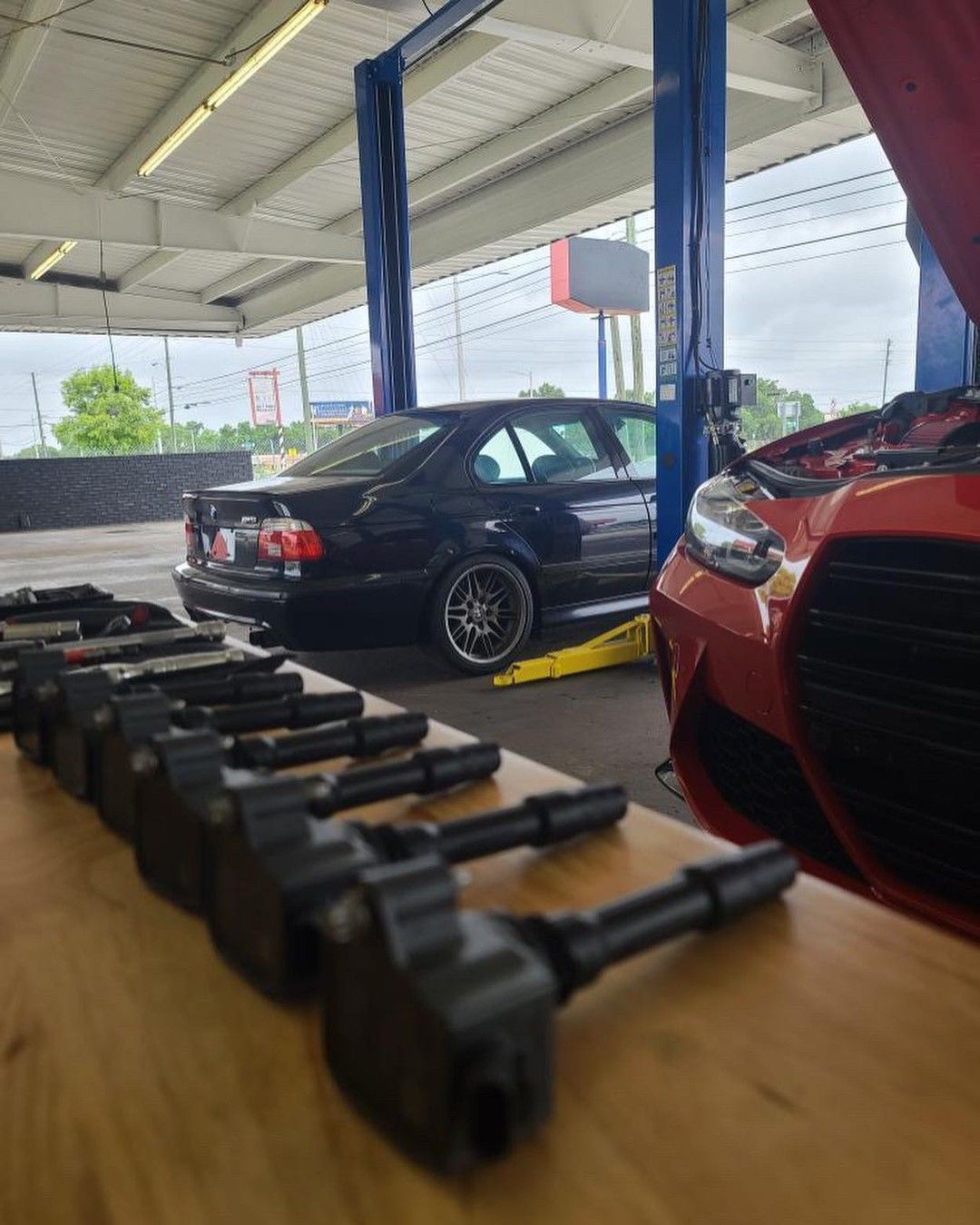 A black car is parked in a garage next to a red car.