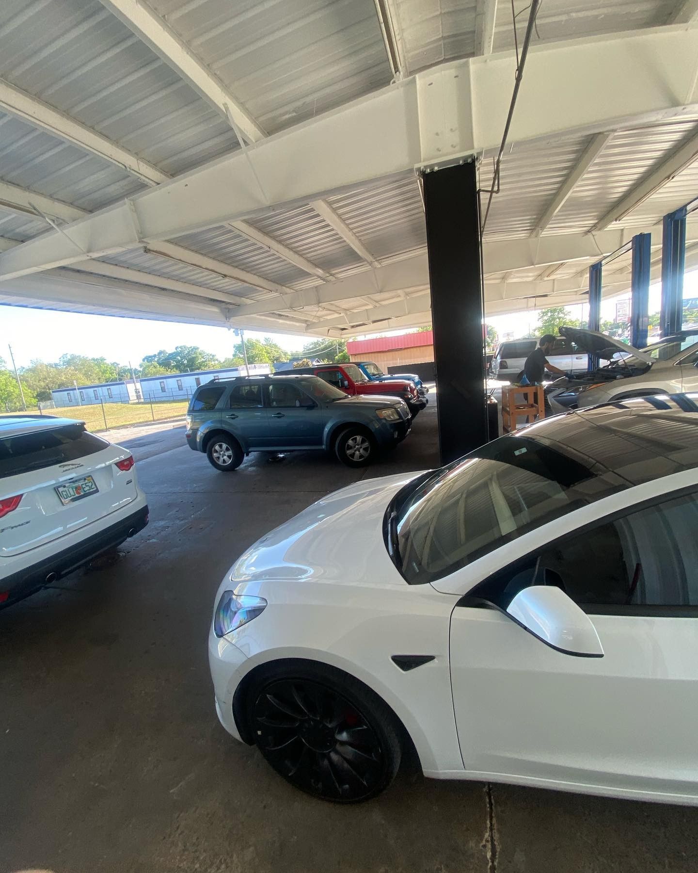 A lot of cars are parked under a roof in a parking lot.
