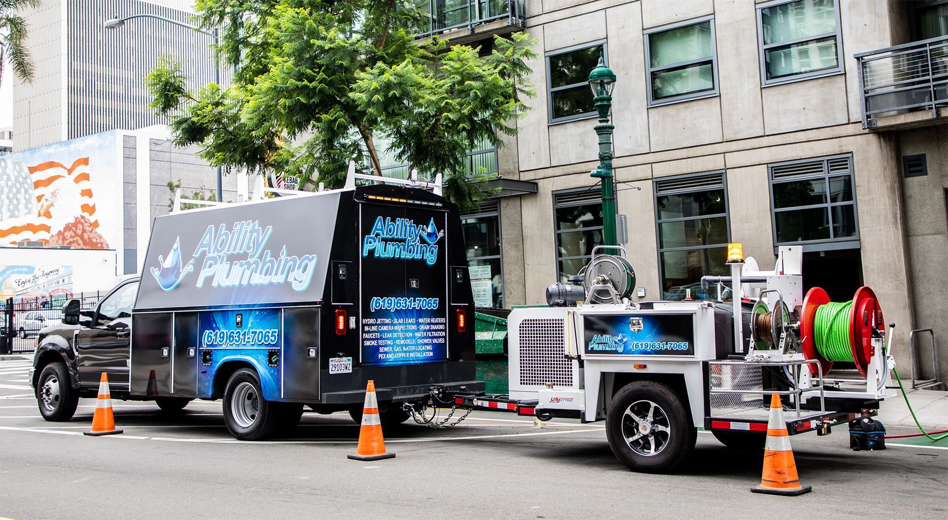 Two plumbing trucks are parked on the side of the road in front of a building.