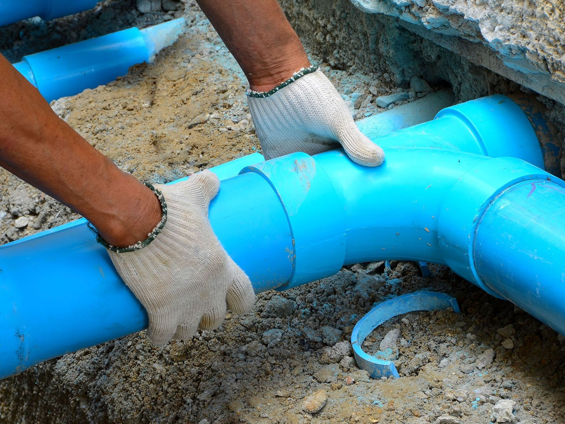 A person is working on a blue pipe in the dirt.