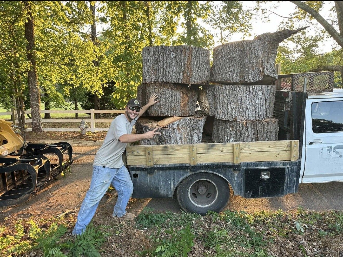 Man pointing at stacked tree trunk sections on a truck bed in a sunny outdoor setting.