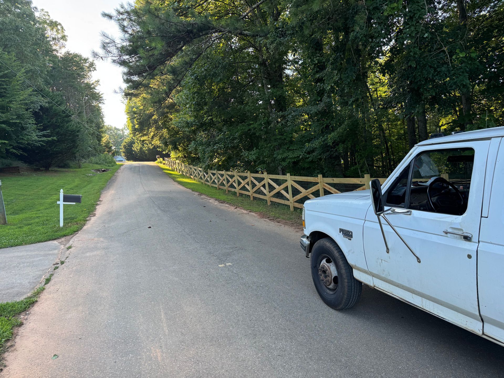 White pickup truck parked on a residential street with a new wooden fence on the side.