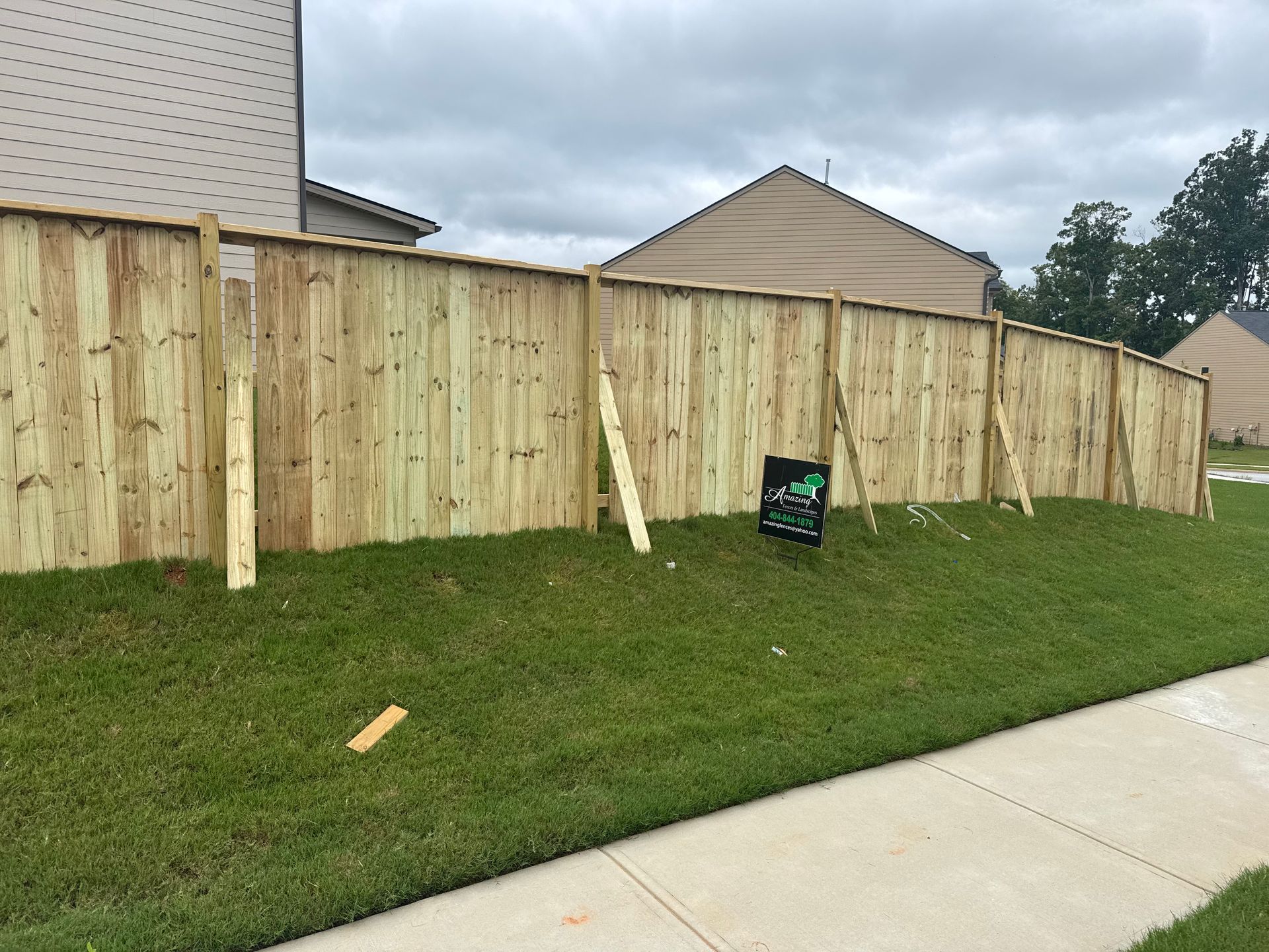 A newly built wooden fence in a yard with supporting beams on a cloudy day.