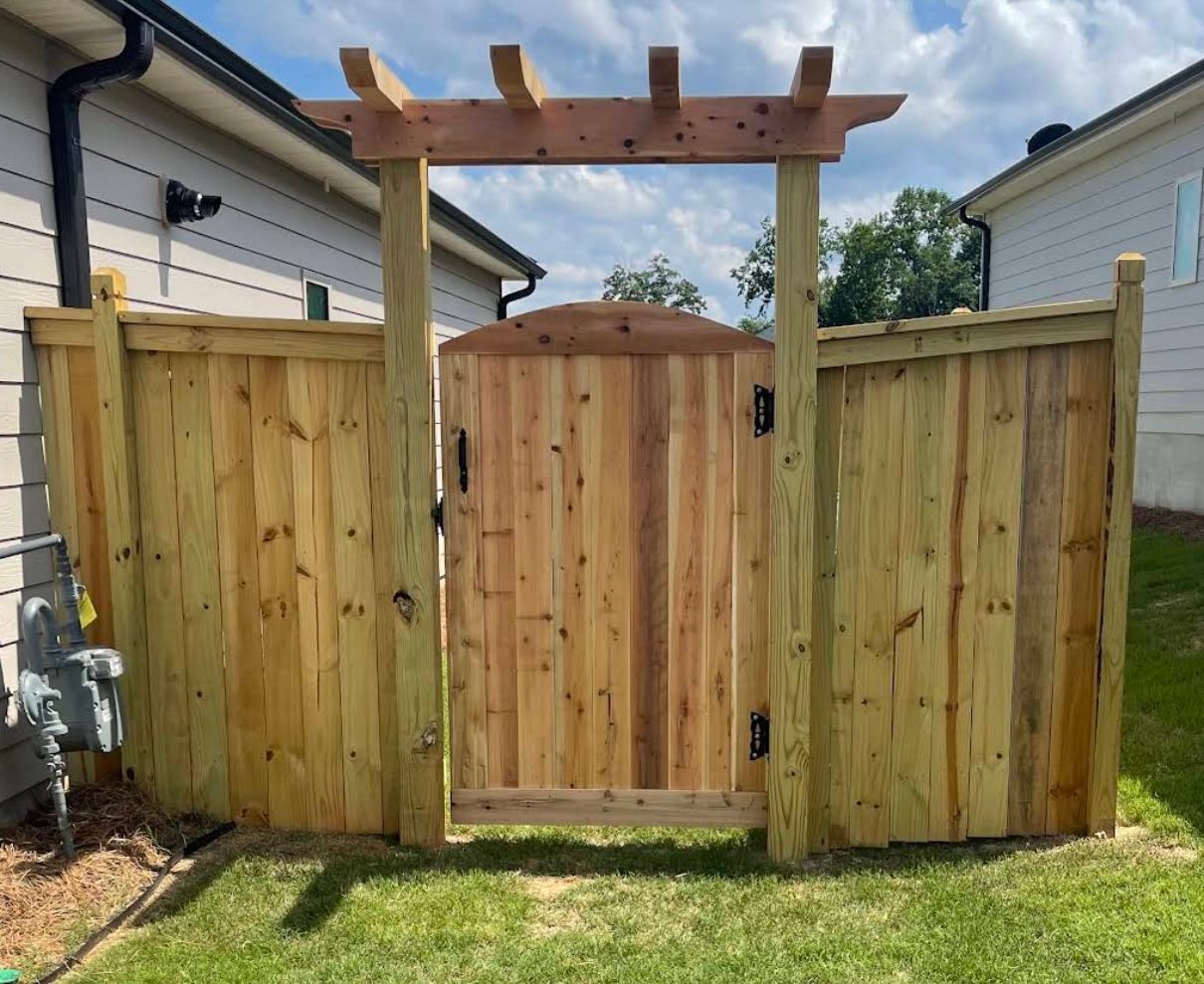 Wooden gate with pergola archway in a backyard, flanked by wooden fences.