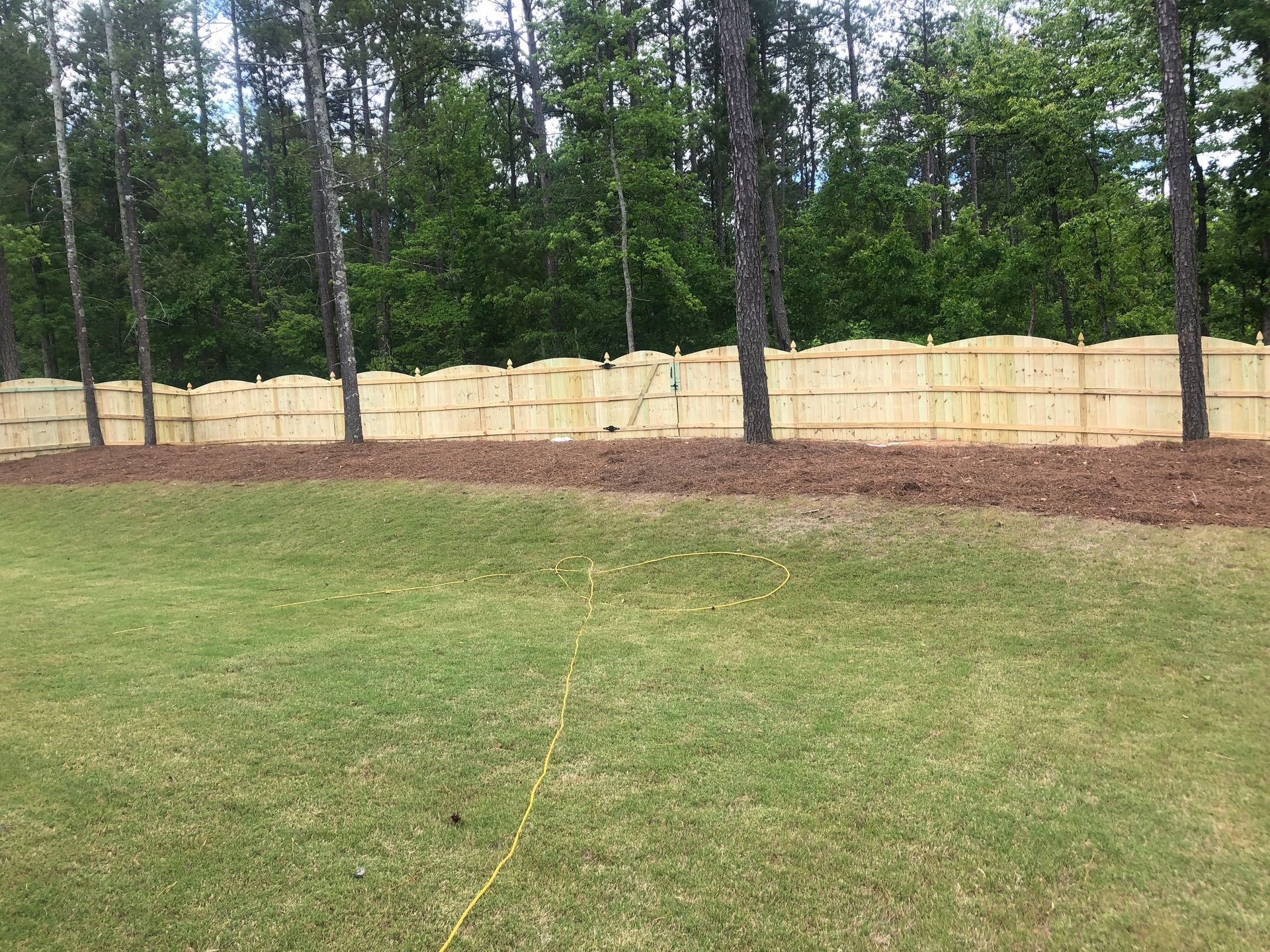 A wooden fence separates a green lawn from a wooded area.