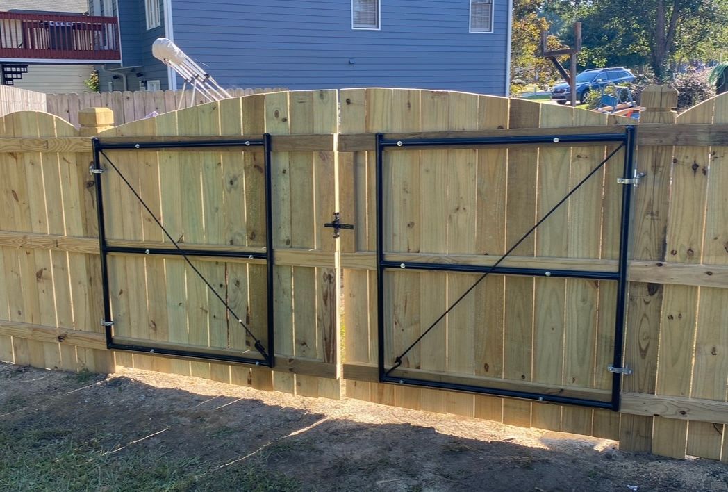 Wooden fence with two black metal gate doors, in a yard.
