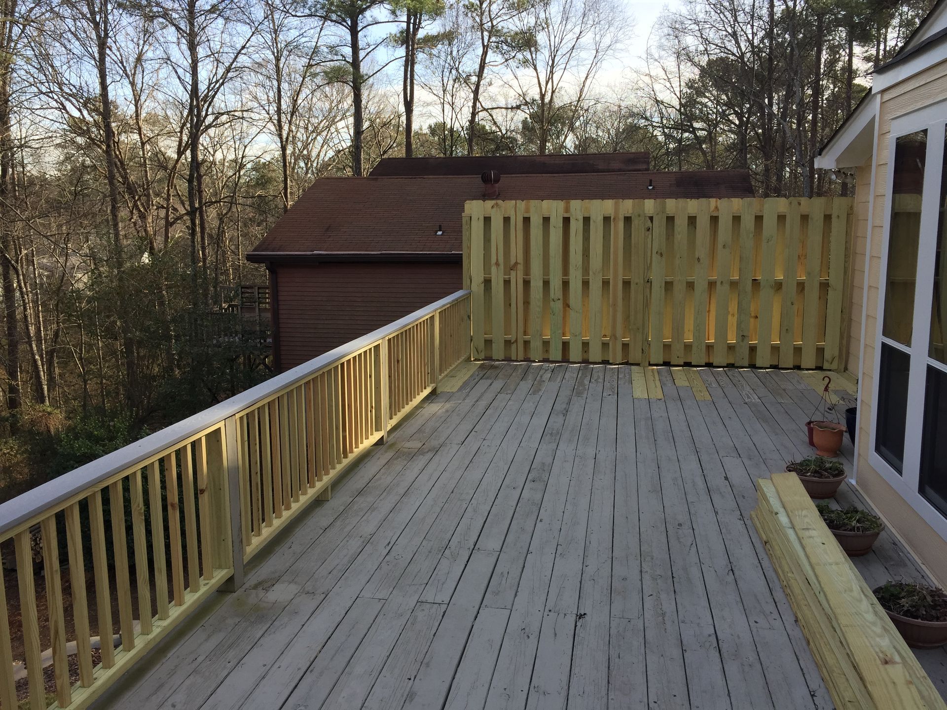 Wooden deck with railing and fence, overlooking trees and a house.