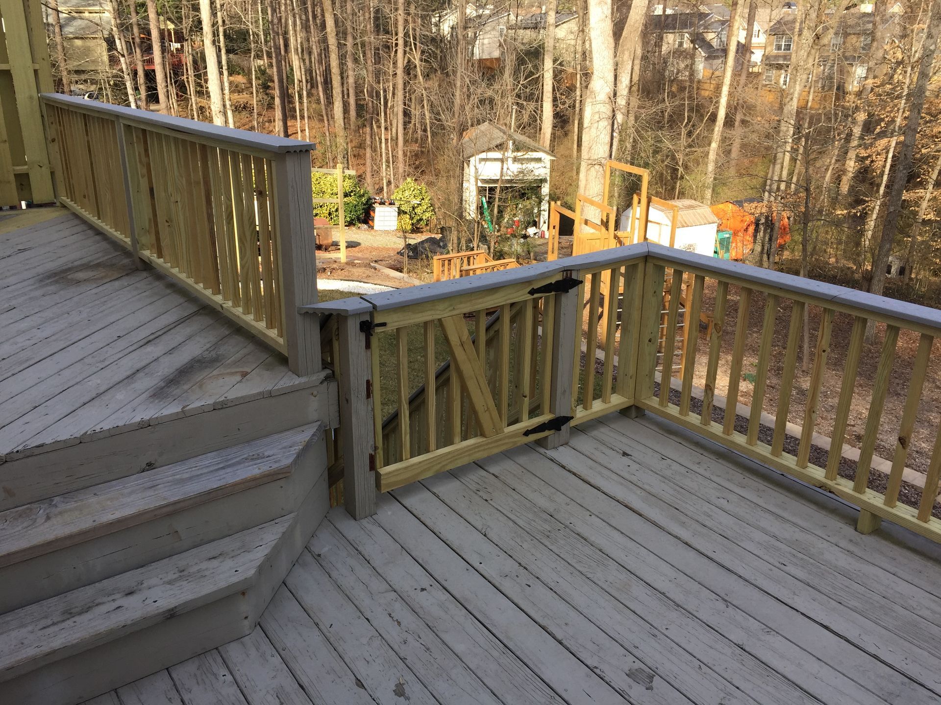 Wooden deck with steps, railings, and a gate, overlooking a backyard with a garden shed.