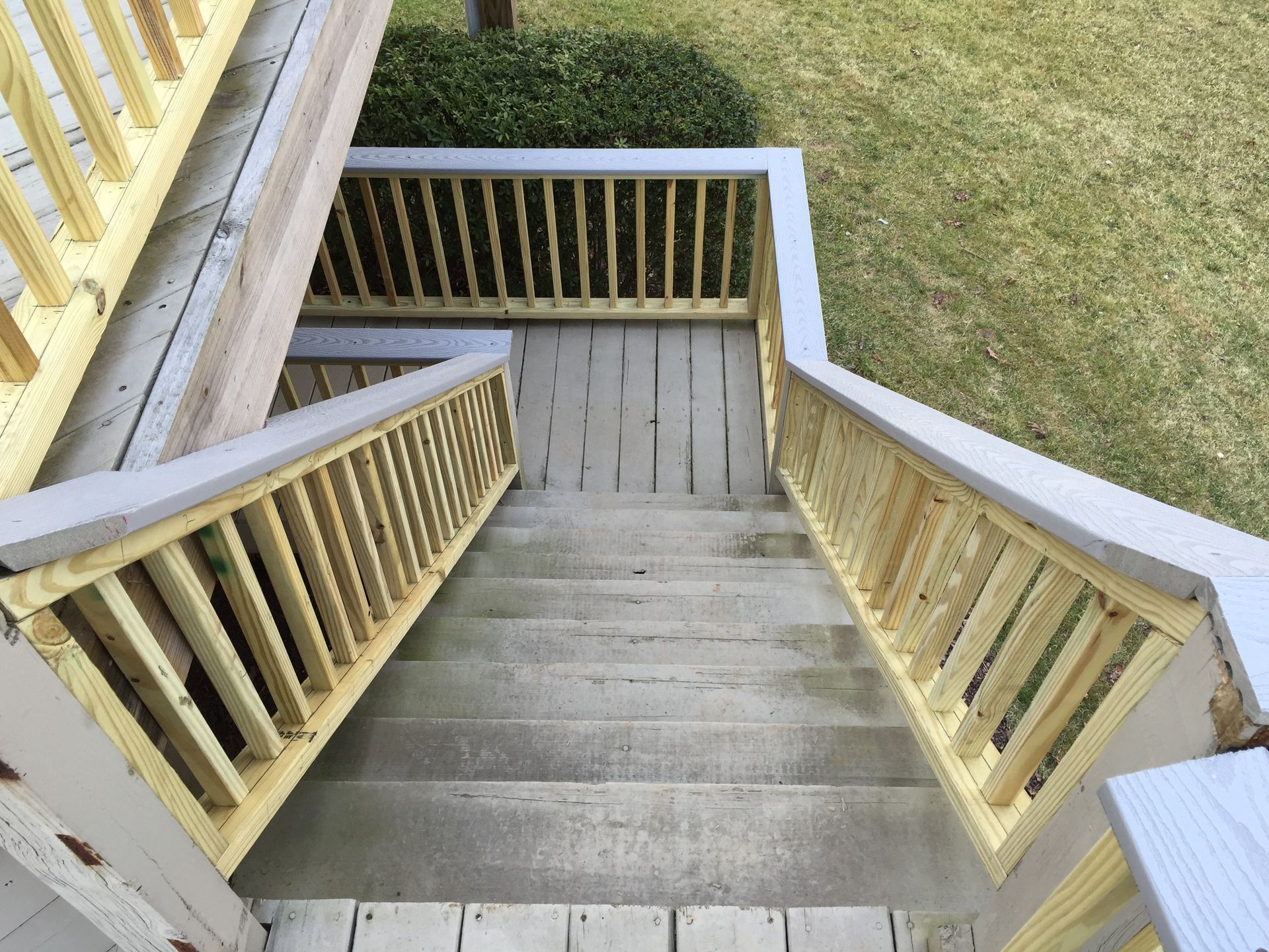 Staircase with wooden railings painted yellow and gray, leading down to a lawn.