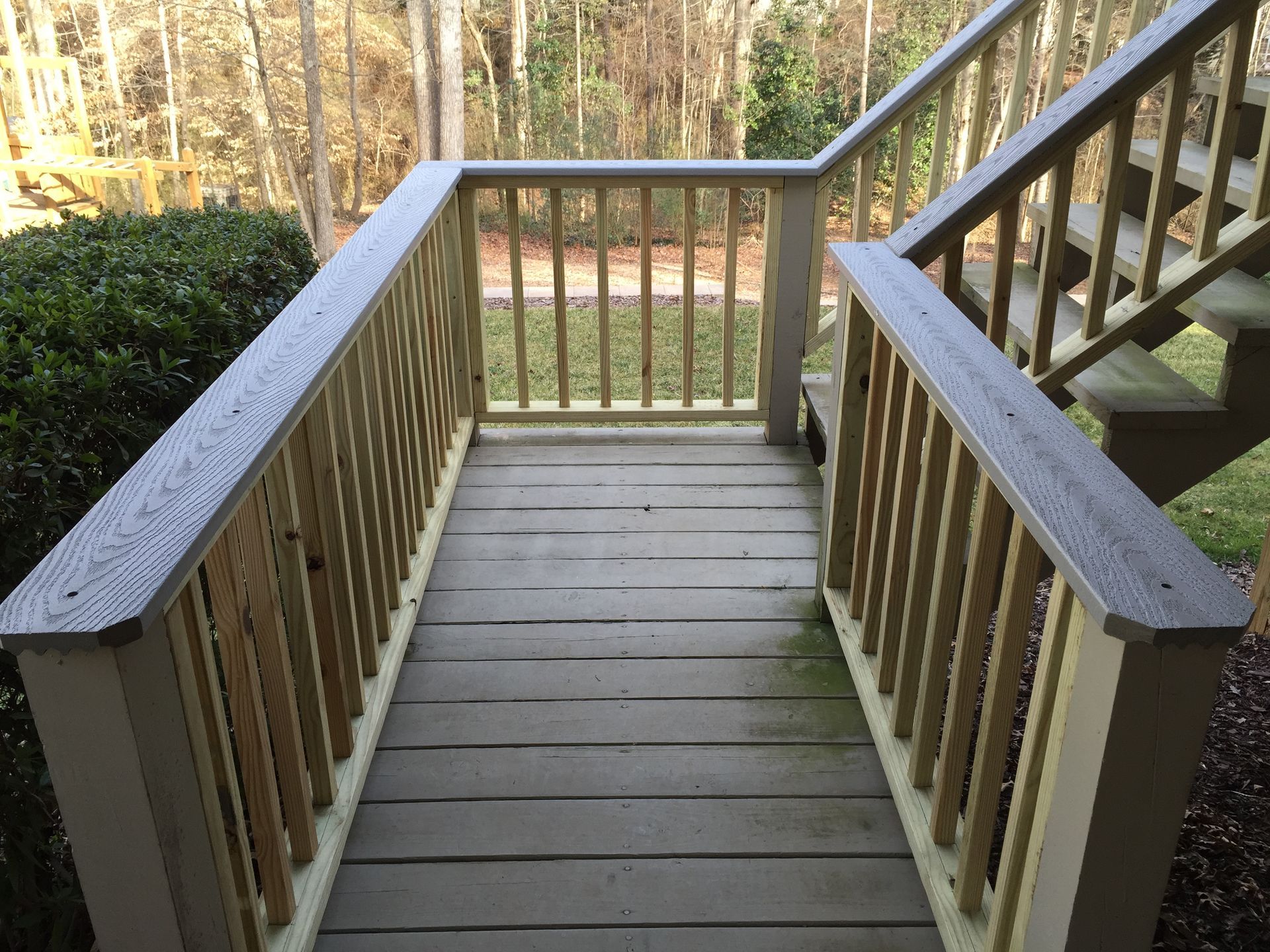 Wooden deck with railings and stairs leading into a wooded area.