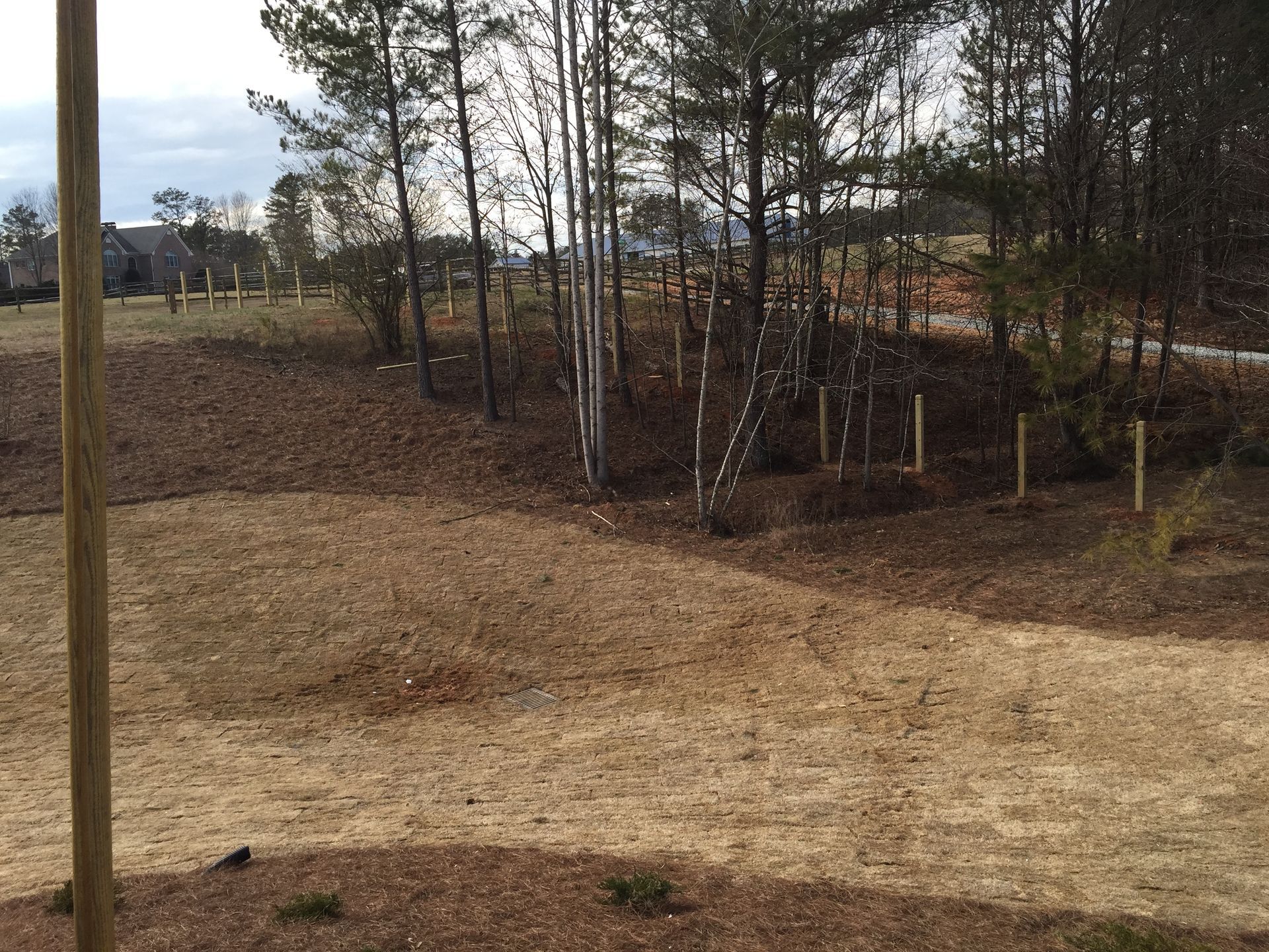 A brown, grassy field with scattered trees and wooden posts. The sky is visible in the background.