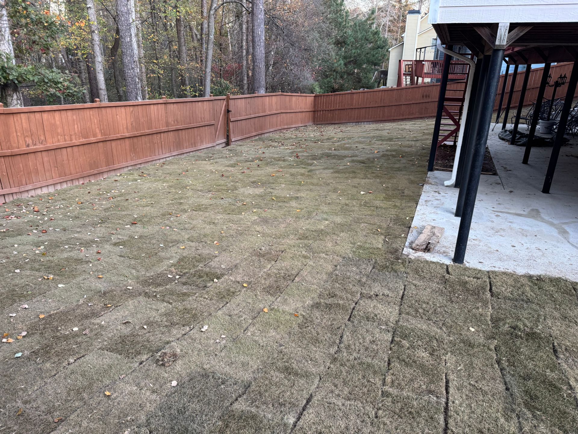 Brown fence surrounds a grassy yard beside a covered porch.